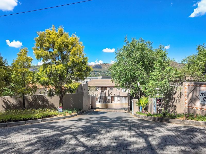 Entrance view of the Macanudo Complex featuring a paved driveway, secure gated access, and perimeter walling.