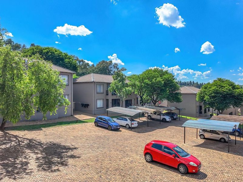An elevated view of the apartment complex exterior, featuring paved parking areas with covered carports and well-maintained multi-story residential buildings.