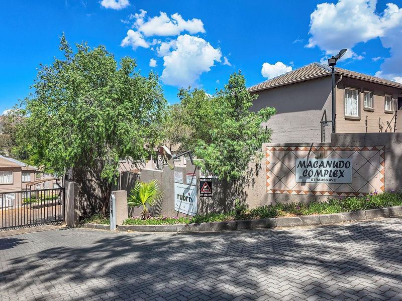 Front entrance view of Macanudo Complex featuring a paved driveway, secure gated access, and perimeter wall with electric fencing.