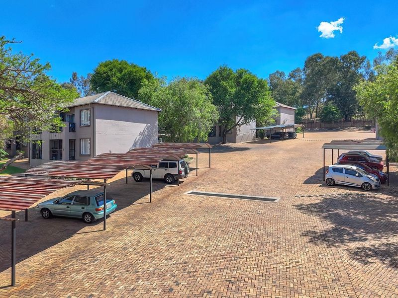 Exterior view of the apartment complex featuring a paved parking area with multiple covered carport structures.