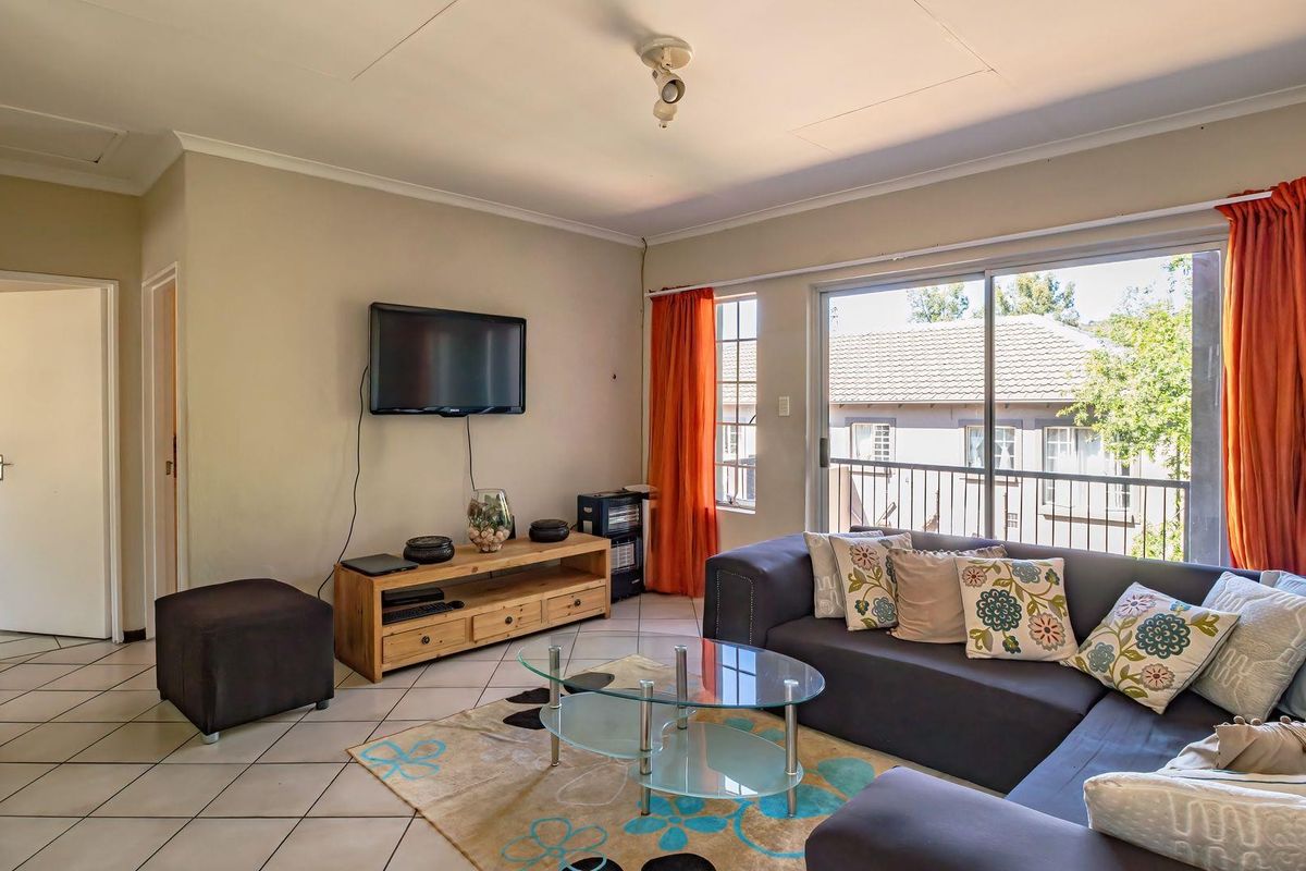 A comfortable living room featuring tiled flooring and a large sliding glass door that provides access to a balcony, allowing for natural light.