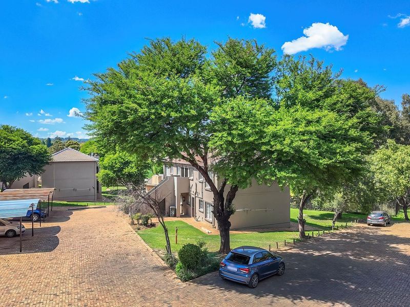 Aerial view of the apartment complex grounds featuring paved parking areas, covered carports, and established garden landscaping.