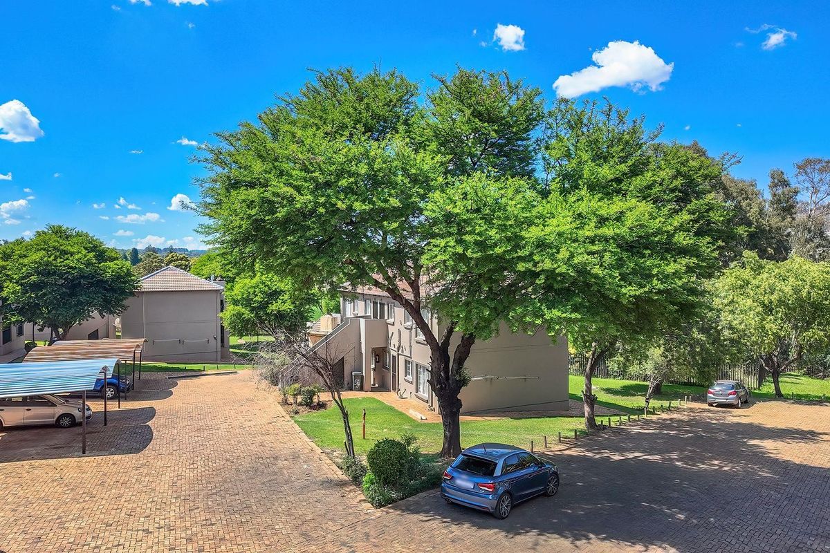 Aerial view of the apartment complex grounds featuring paved parking areas, covered carports, and established garden landscaping.