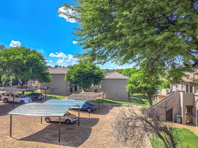An elevated view of the apartment complex grounds featuring paved parking areas with covered carports, mature trees, and well-maintained building exteriors.