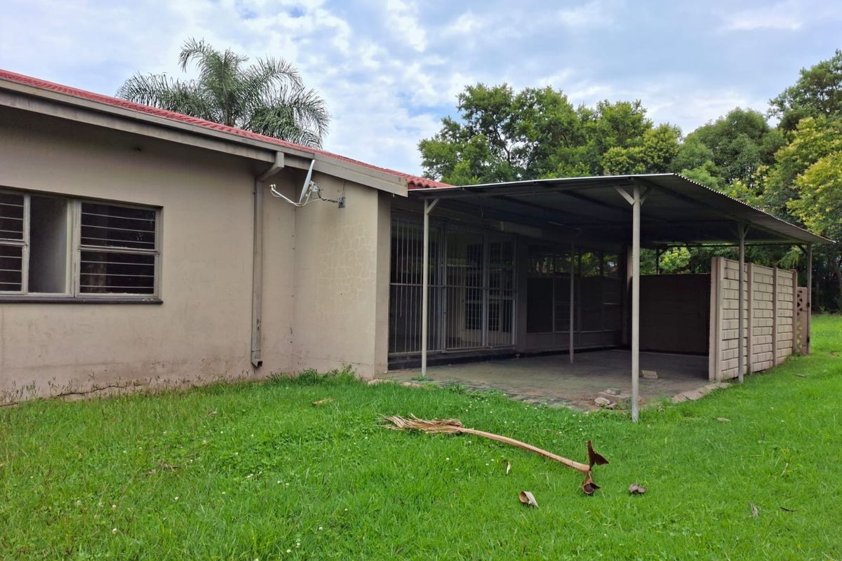 Rear view of the property featuring a covered patio area, security bars on windows, and a large garden space with a brick boundary wall.