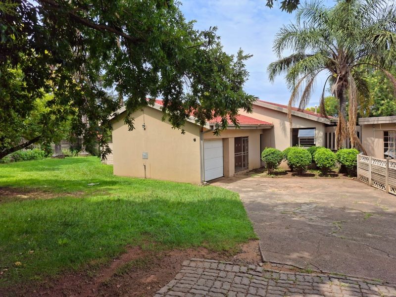 Front view of the property featuring a concrete driveway, single garage, and established garden area with mature trees.
