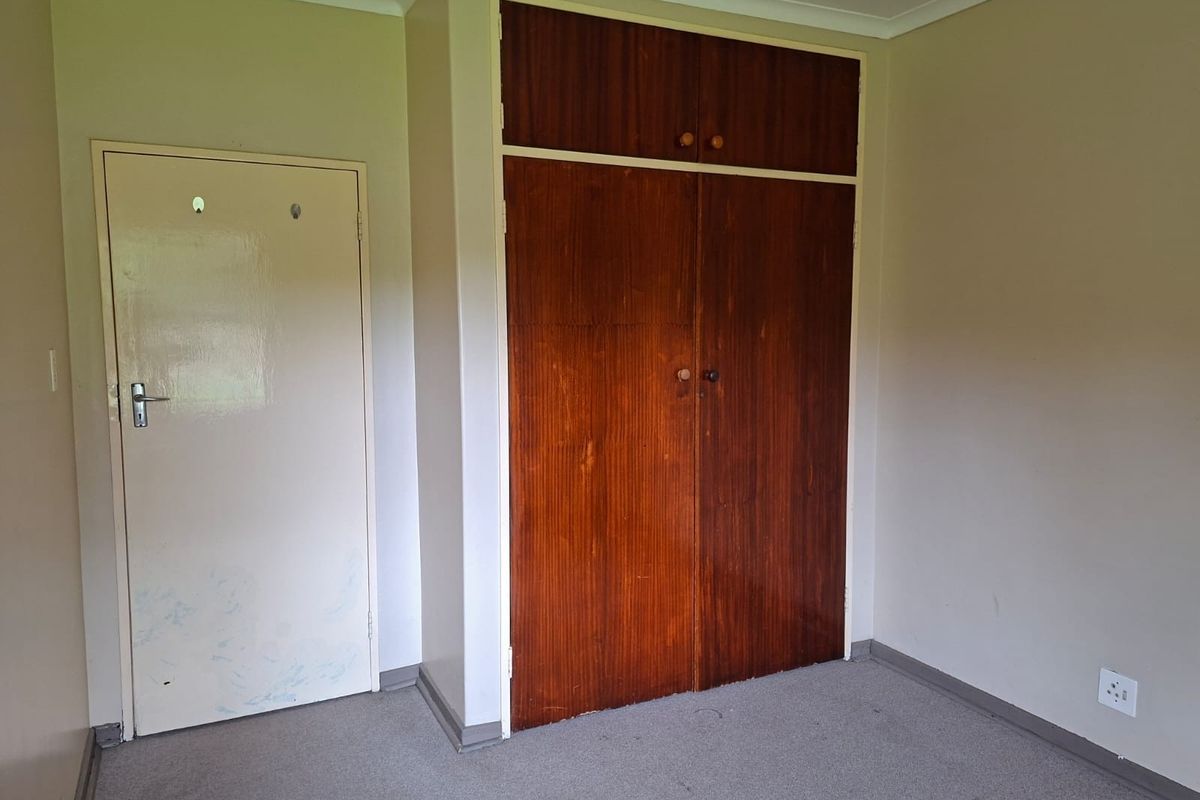 A vacant bedroom featuring a built-in wooden wardrobe, neutral wall paint, and carpet flooring, offering a blank canvas for potential updates.