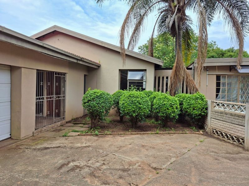 Front exterior view of the house featuring a concrete driveway, security gate, and established garden area with weathered exterior finishes.