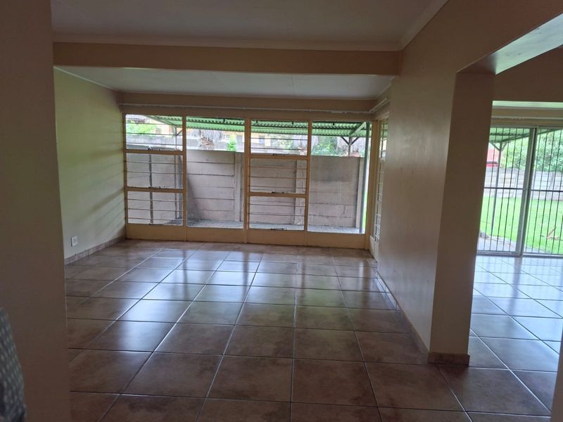 Spacious, empty living area featuring neutral tiled flooring and large windows that provide ample natural light and access to the outdoor space.