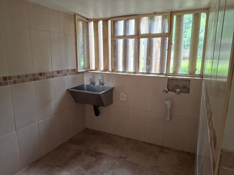 A functional laundry area featuring a stainless steel utility sink, tiled finishes, and plumbing connections ready for appliance installation.