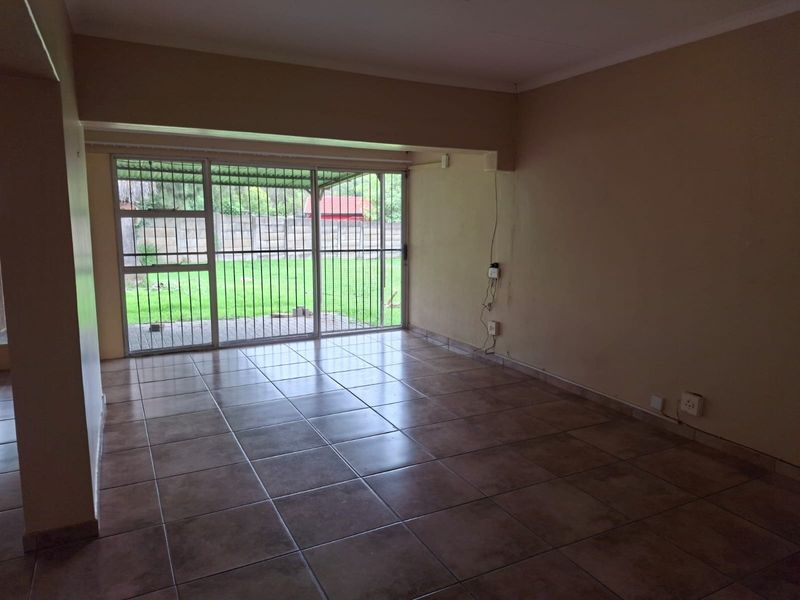 An empty living room featuring tiled flooring and a large sliding glass door with security bars, providing direct access to the rear garden area.
