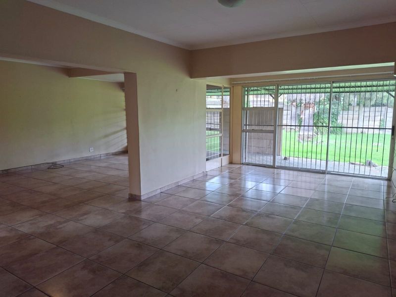 Spacious open-plan living area featuring neutral tiled flooring and large sliding glass doors with security bars, providing direct access to the rear garden.