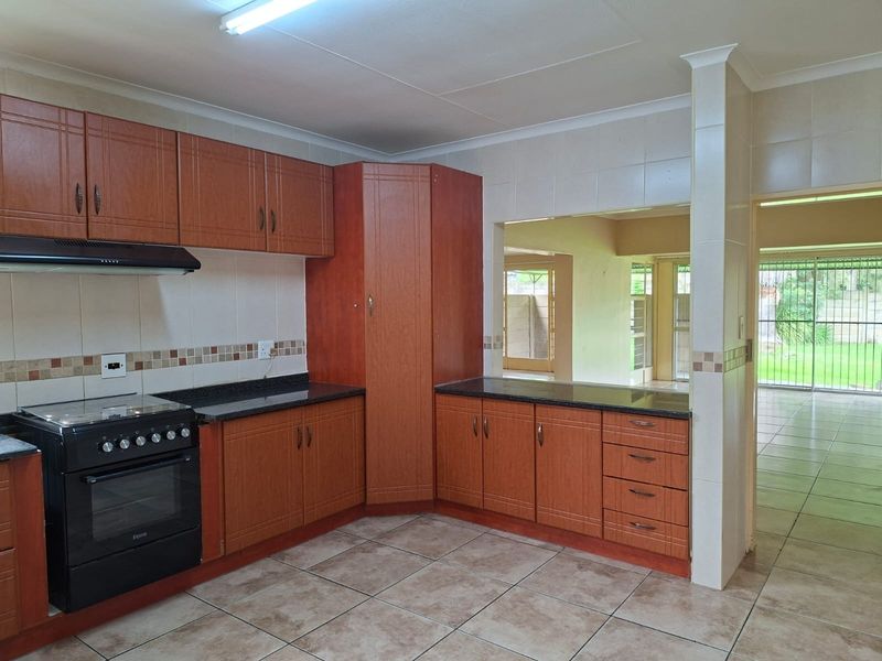 A functional kitchen featuring wood-finish cabinetry, granite countertops, a freestanding stove with extractor, and tiled flooring, with a convenient pass-through window to the living area.