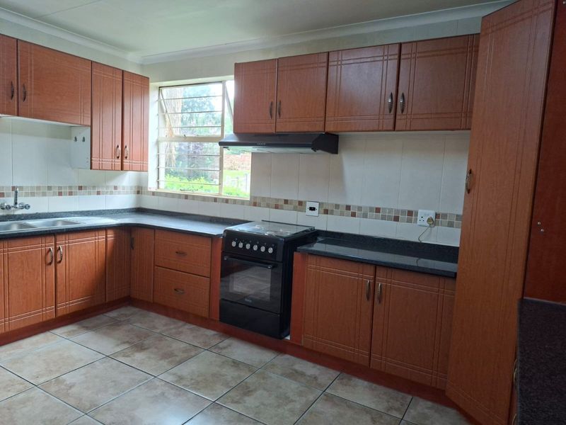 A functional kitchen featuring wood-look laminate cabinetry, granite countertops, tiled backsplash, and a freestanding stove with an extractor fan.