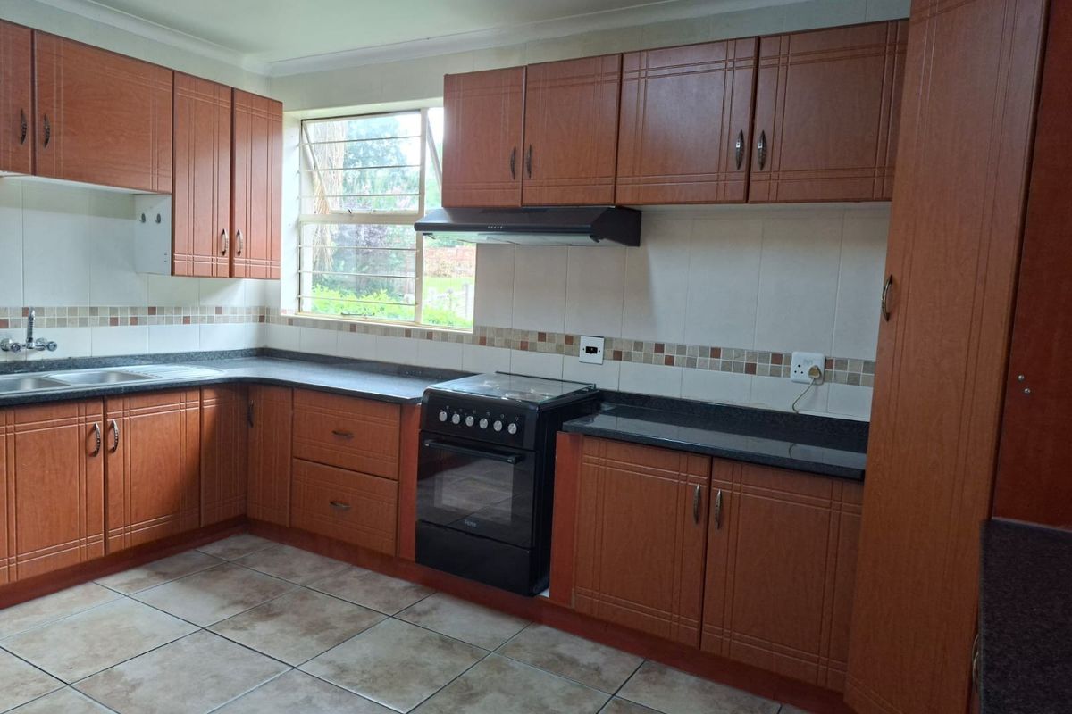 A functional kitchen featuring wood-look laminate cabinetry, granite countertops, tiled backsplash, and a freestanding stove with an extractor fan.