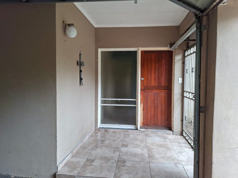 A covered entrance area featuring tiled flooring, a solid wooden front door with a glass sidelight, and a security gate.