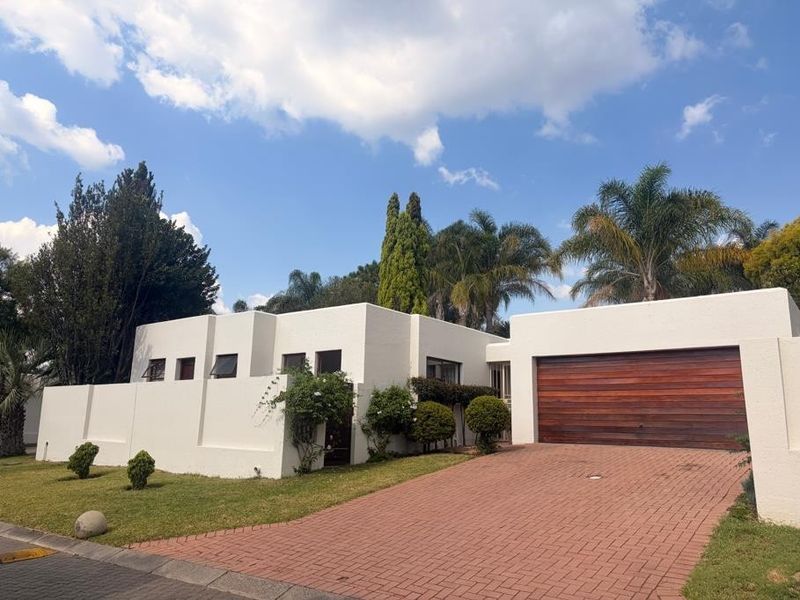 Front exterior view of a modern house featuring a paved driveway, a wooden garage door, and a well-maintained boundary wall and garden.