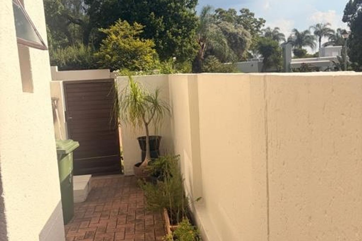 A side pathway featuring paved flooring, a high boundary wall, and a secure pedestrian gate leading to the rear garden area.
