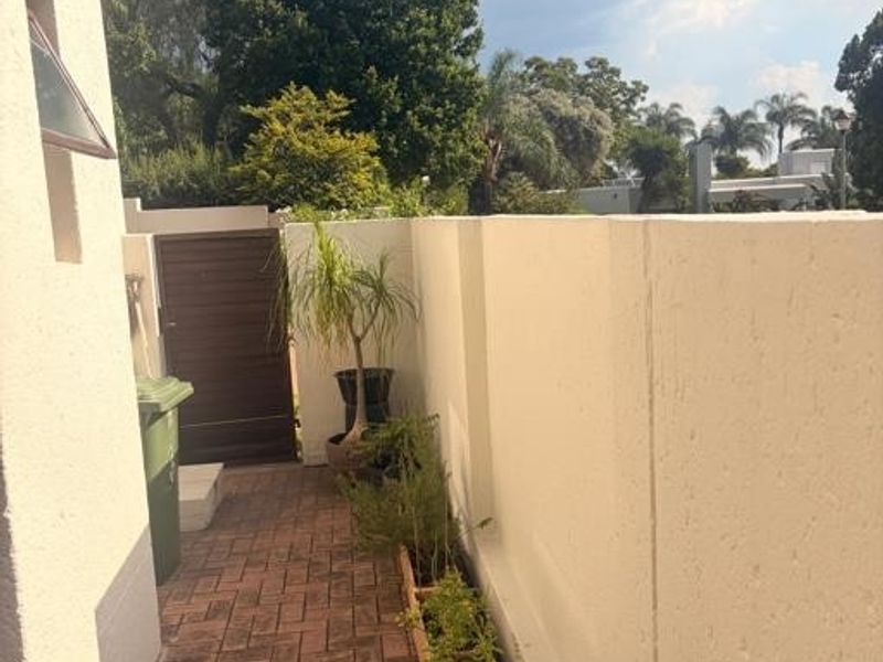 A side pathway featuring paved flooring, a high boundary wall, and a secure pedestrian gate leading to the rear garden area.