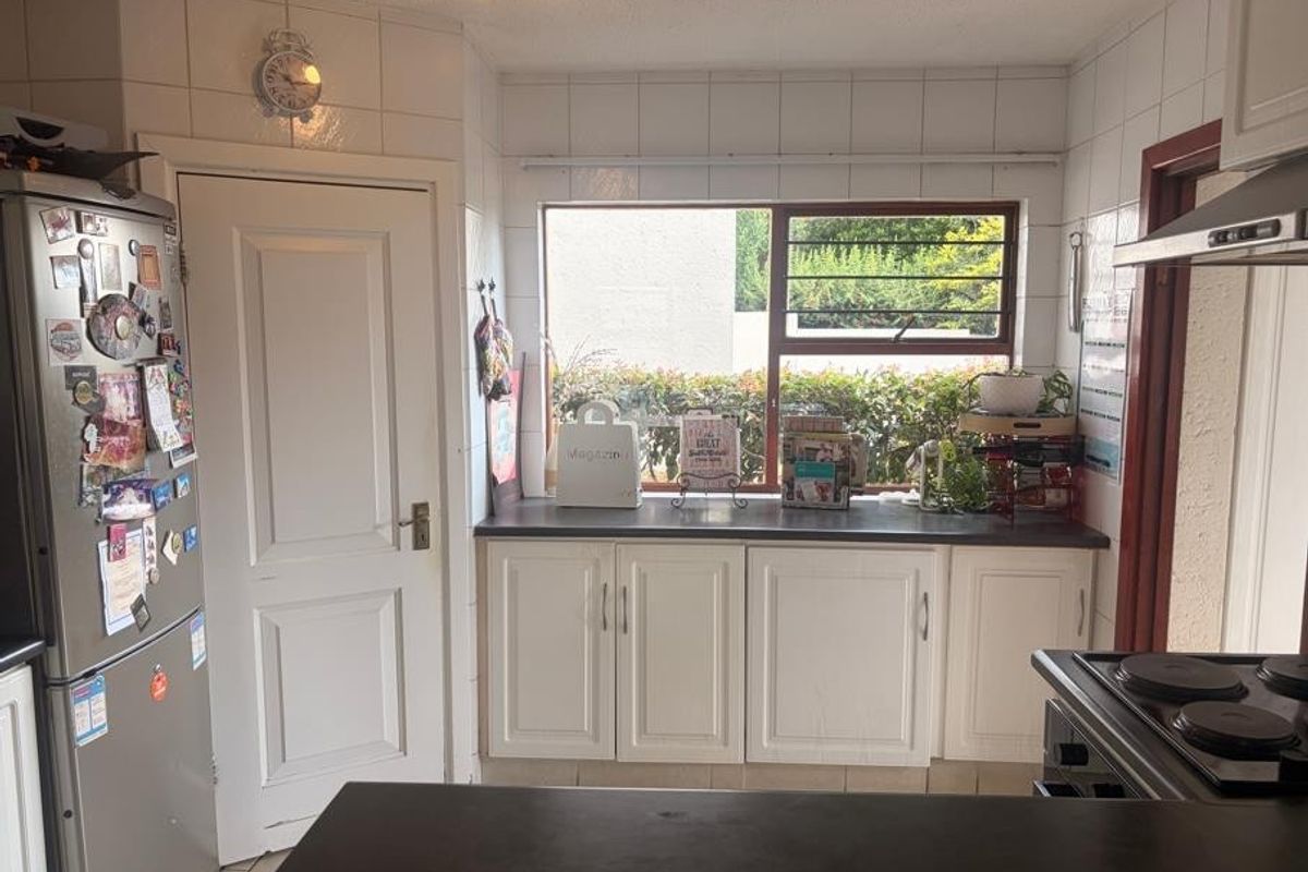 A functional kitchen featuring white cabinetry, dark laminate countertops, a tiled splashback, and an electric hob with an extractor fan.