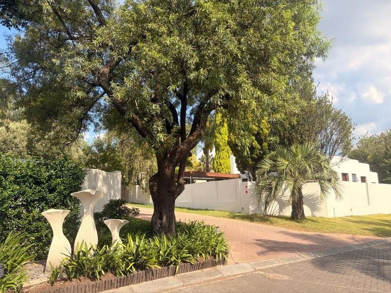 A well-maintained front exterior view featuring a paved driveway, established garden landscaping, and a secure boundary wall.