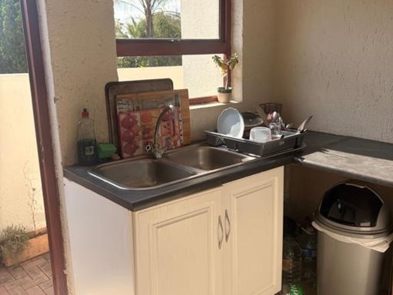 A functional scullery area featuring a double bowl stainless steel sink, built-in cabinetry, and tiled flooring, providing a practical space for wash-up tasks.