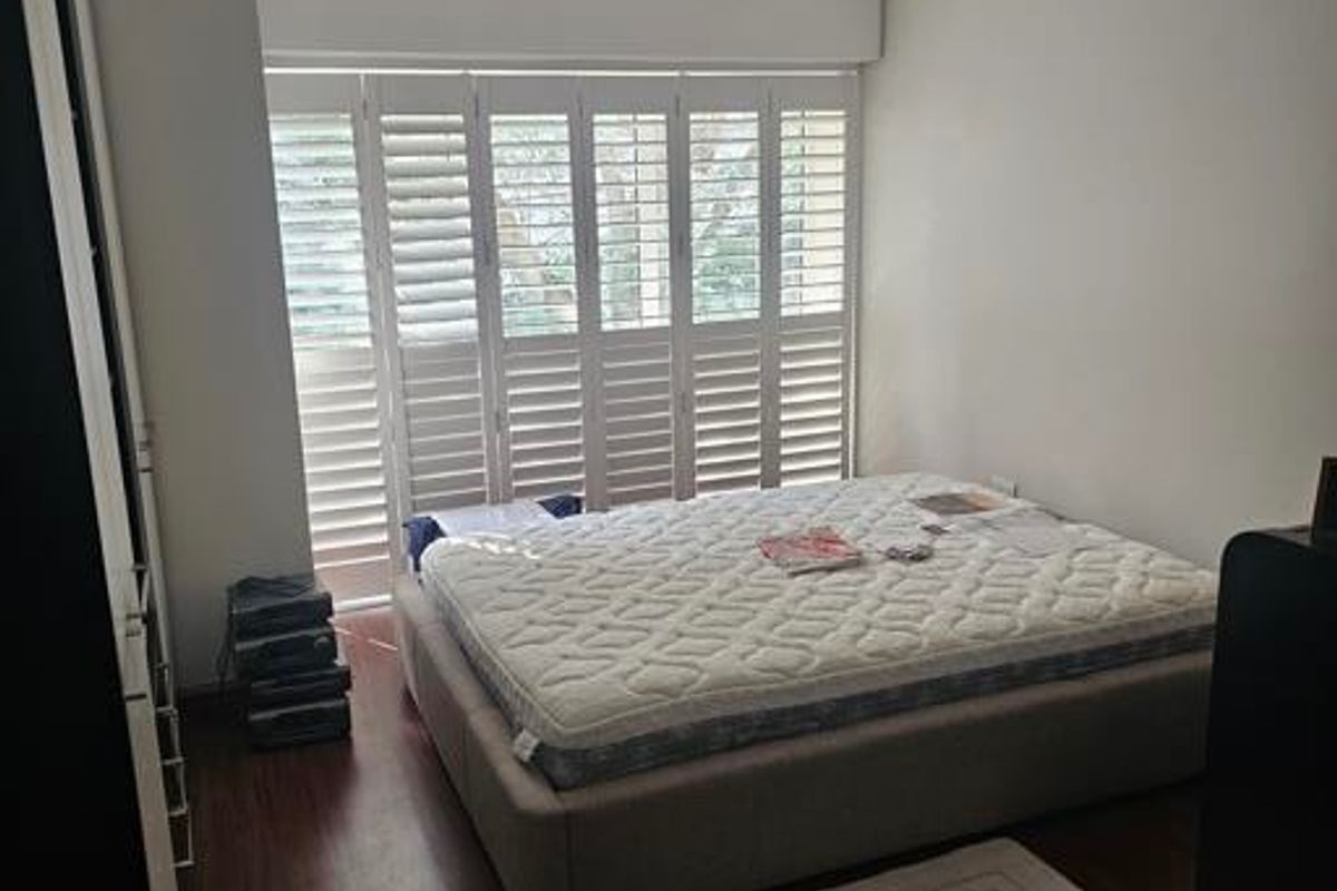 A well-lit bedroom featuring dark laminate flooring, built-in cupboards, and white plantation shutters providing natural light control.