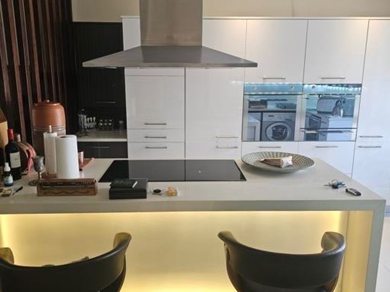 Modern kitchen featuring a central island with an induction hob, built-in appliances, sleek gloss cabinetry, and integrated under-counter lighting.