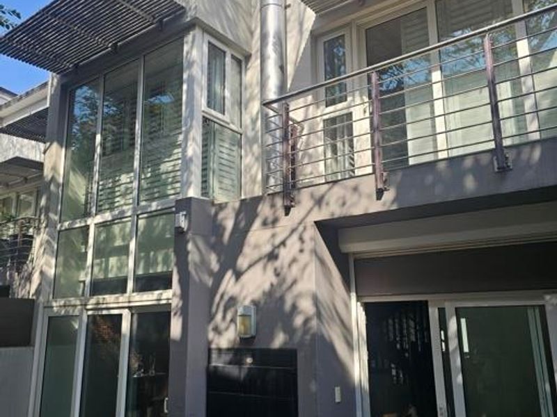 Rear elevation of a modern townhouse featuring a built-in braai, balcony with stainless steel railing, large sliding glass doors, and metal sun louvres.
