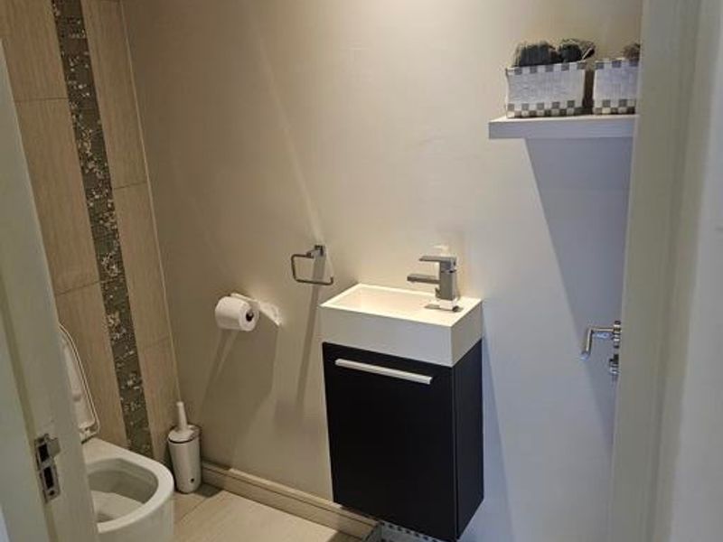 A compact guest bathroom featuring a wall-mounted toilet, modern vanity with basin, and neutral floor tiles with a decorative vertical accent wall.