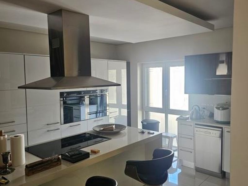 Modern kitchen featuring a central island with an induction hob, stainless steel extractor fan, built-in oven, and sleek gloss cabinetry with tiled flooring.