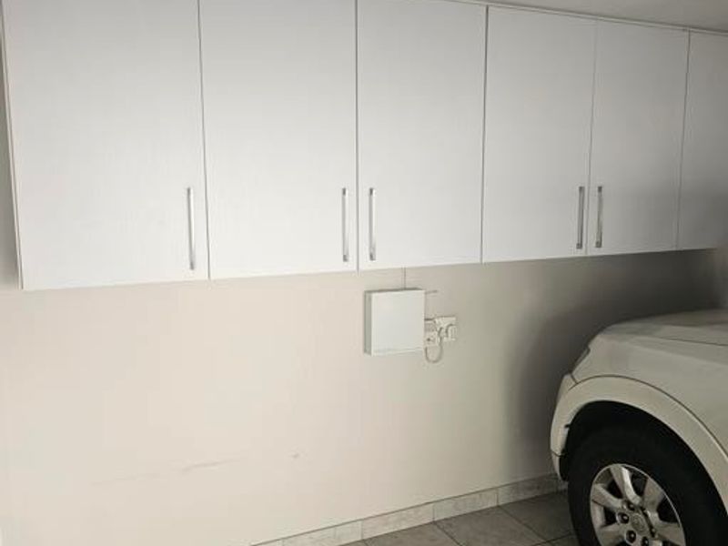 A functional garage space featuring extensive built-in white wall cabinetry for storage and durable tiled flooring.