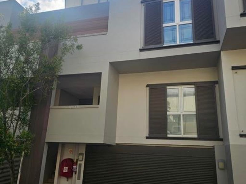 Front elevation of a modern townhouse featuring a secure roller garage door, dark louvred window shutters, and a paved driveway entrance.