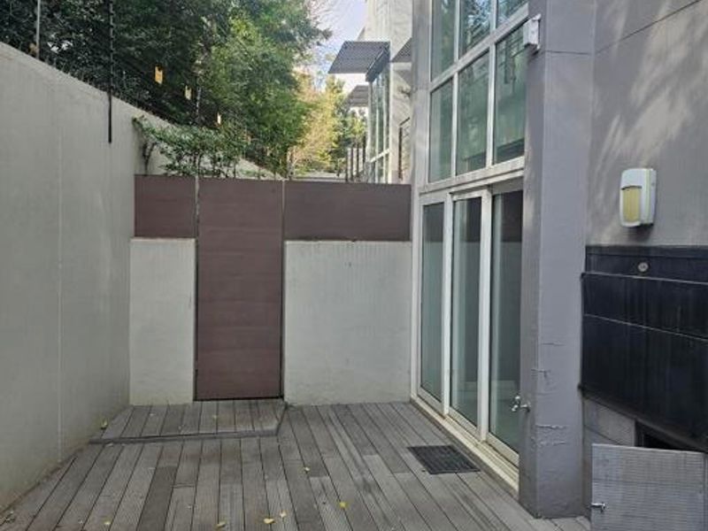 A private outdoor patio featuring timber decking, a built-in braai, and full-height glass doors leading into the townhouse interior.