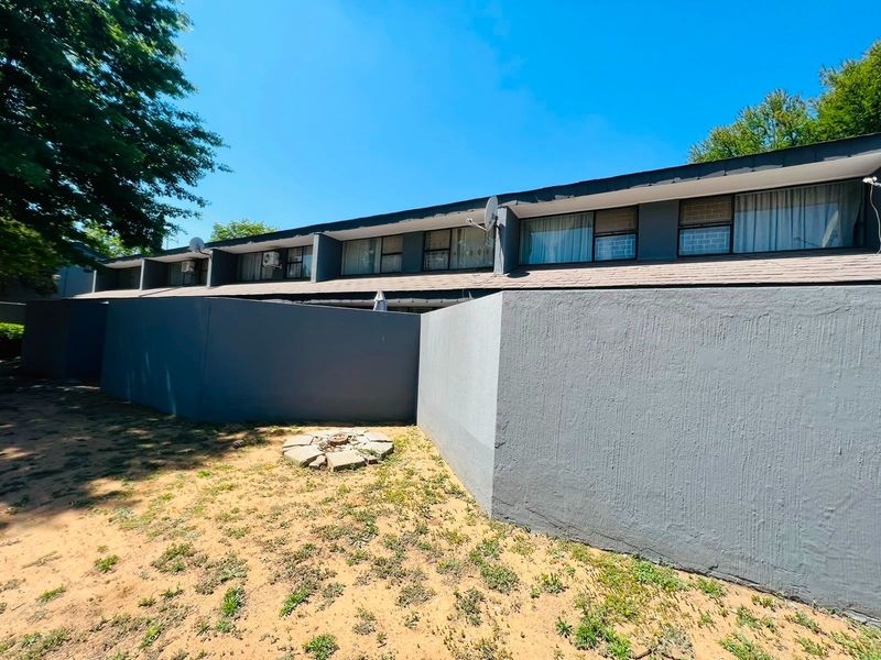 Rear view of the townhouse featuring a private garden area with boundary walls and exterior air conditioning units.