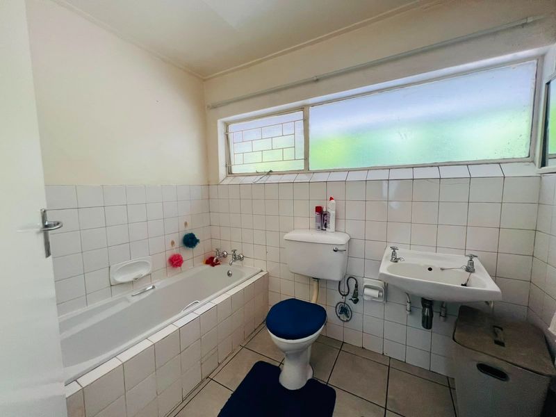 A functional bathroom featuring a built-in bathtub, pedestal washbasin, and toilet, finished with classic white wall tiles and neutral floor tiling.