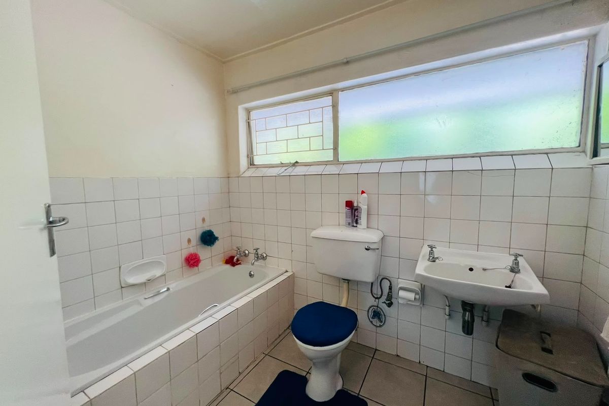 A functional bathroom featuring a built-in bathtub, pedestal washbasin, and toilet, finished with classic white wall tiles and neutral floor tiling.