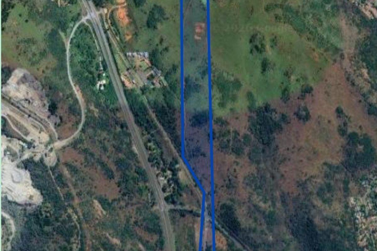 Aerial satellite view of a long, narrow commercial vacant land plot with boundary lines highlighted.