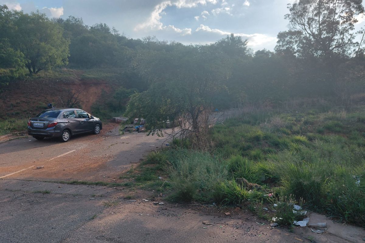 A view of the vacant commercial land featuring an asphalt driveway and sloped, overgrown terrain.