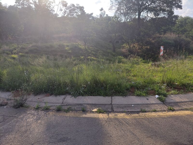 A view of a vacant commercial land plot from the street, featuring a sloped grassy area and concrete curbing.