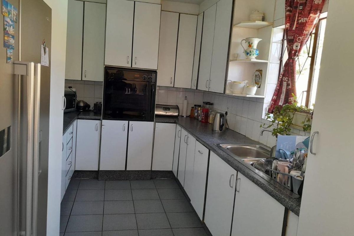 A functional kitchen featuring white built-in cabinetry, laminate countertops, a stainless steel sink, and tiled flooring, offering a practical layout for daily use.
