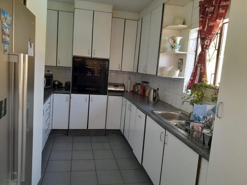 A functional kitchen featuring white built-in cabinetry, laminate countertops, a stainless steel sink, and tiled flooring, offering a practical layout for daily use.