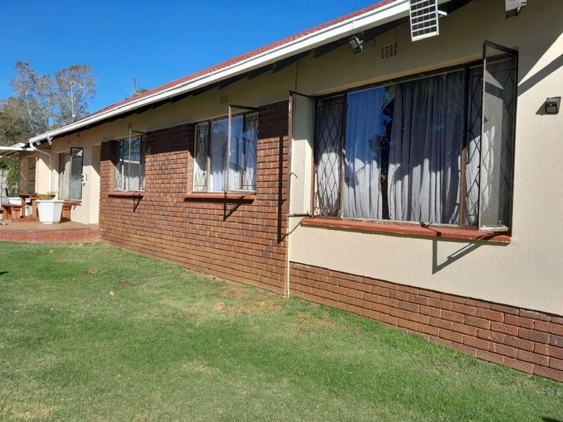 Rear exterior view of the house featuring a brick and plaster facade, metal-framed windows with security bars, and a tiled roof.