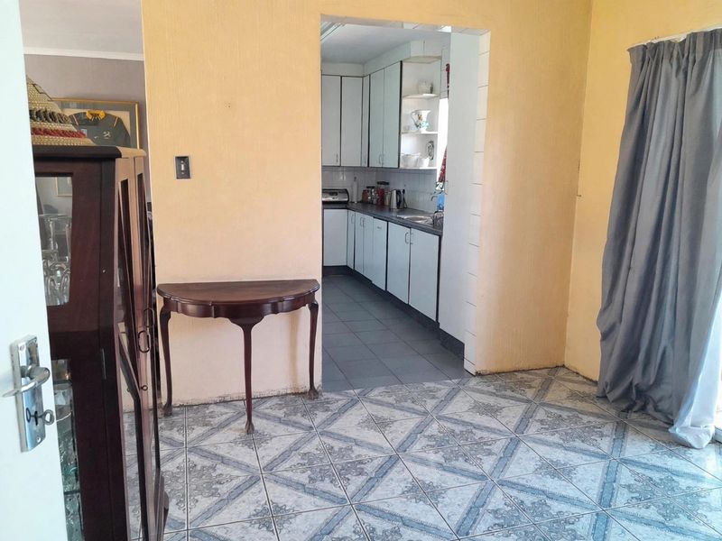 Open plan living area featuring tiled flooring and a separate kitchen space with fitted cabinetry and sink, requiring cosmetic updates.