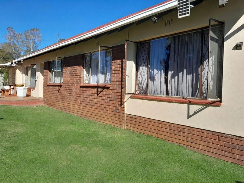 Rear exterior view of the house featuring a brick and plaster facade, metal-framed windows with security bars, and a tiled roof.