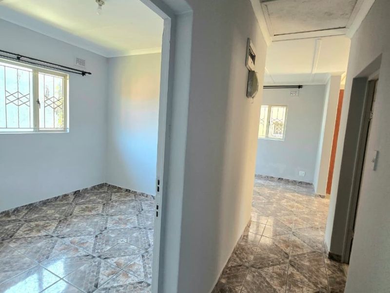 A bright, empty hallway featuring tiled flooring and access to adjacent rooms, with security bars installed on the windows.