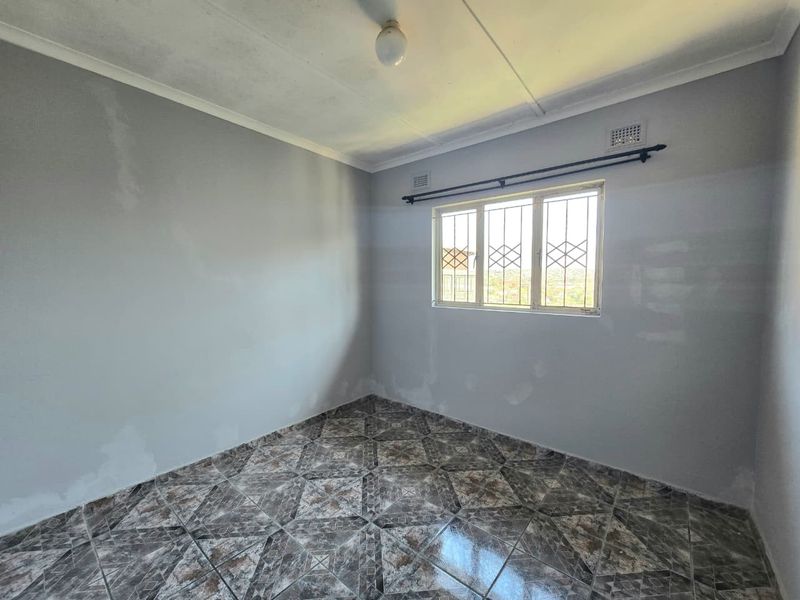 An empty bedroom featuring tiled flooring, security bars on the window, and a neutral wall finish, ready for personalization.