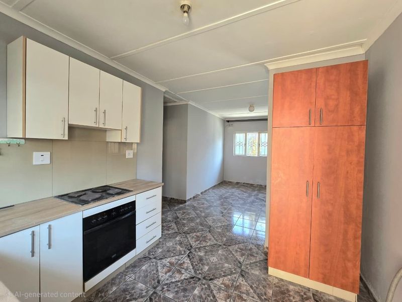 Open-plan kitchen and living area featuring tiled flooring, built-in cabinetry with integrated oven and hob, and a tall storage cupboard.