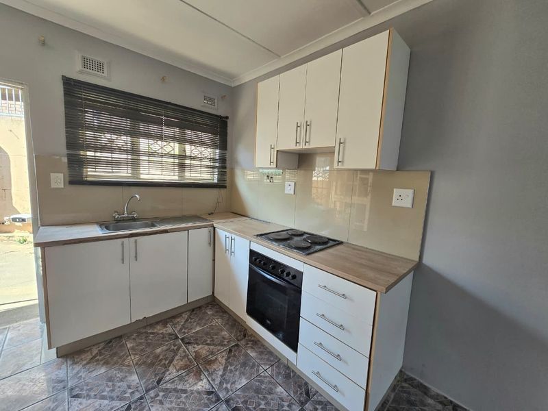 A clean and functional kitchen featuring white cabinetry, wood-look laminate countertops, a built-in oven, electric hob, and tiled flooring.