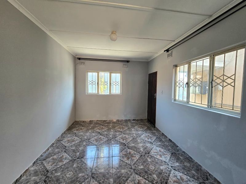 An empty living room featuring tiled flooring, security bars on the windows, and neutral wall finishes, offering a blank canvas for interior design.
